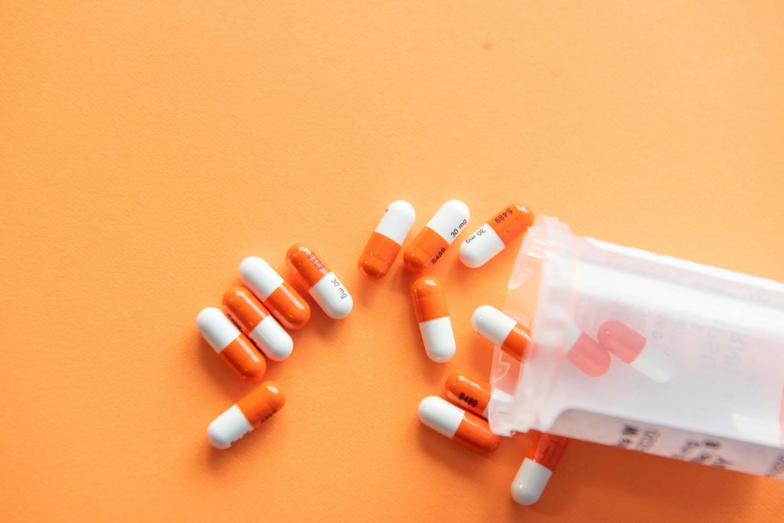 A Bottle Of Orange And White Capsules Spilled Out On An Orange Background