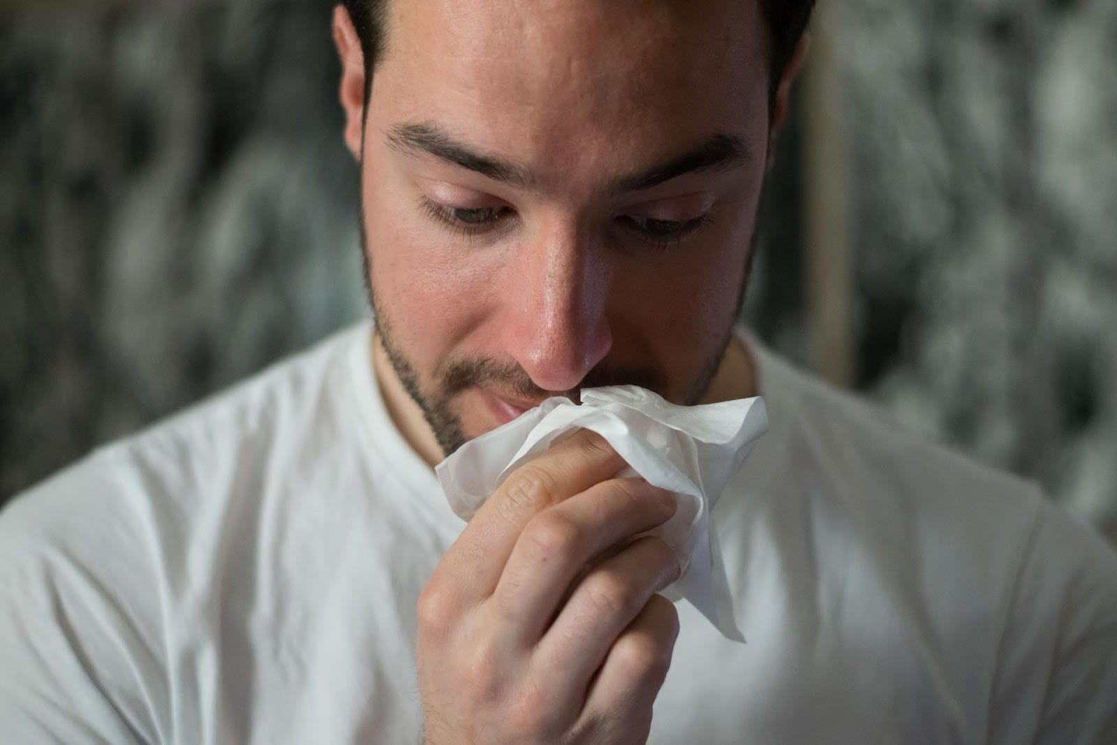 A Man Holding A Tissue To His Nose Looking Down