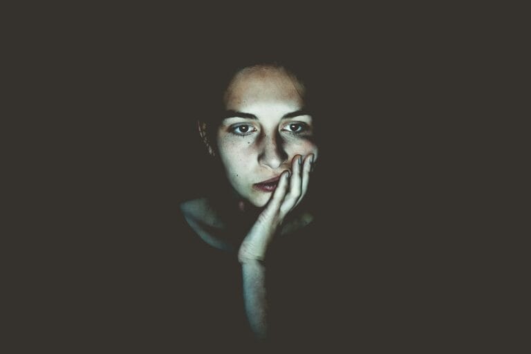 A woman sitting in the dark with her head resting on her hand